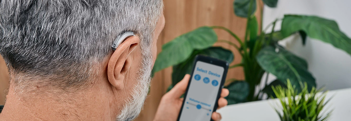Mann mit Hörgerät nutzt Smartphone-App zur Hörgeräte-Einstellung zuhause