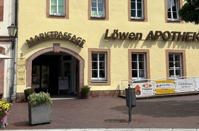 Eingang zur Marktpassage und Löwen Apotheke an gelber Hausfassade mit Blumenschmuck.